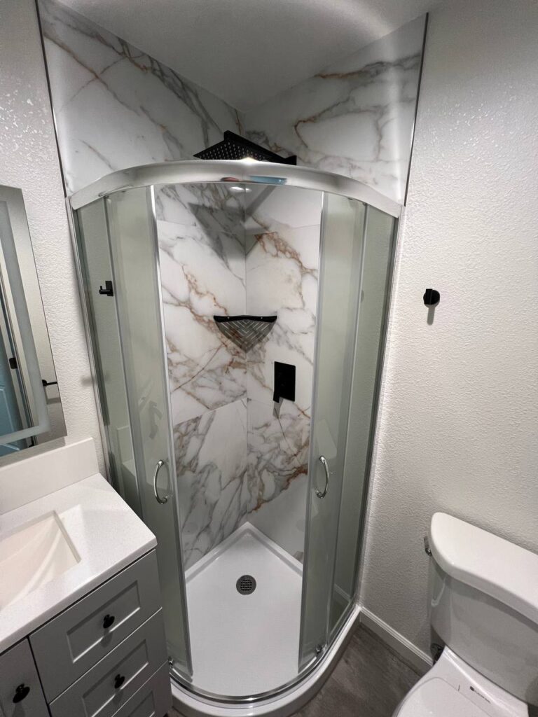 Compact corner shower enclosure with marble-look tile walls and white decorative plaster in a small bathroom