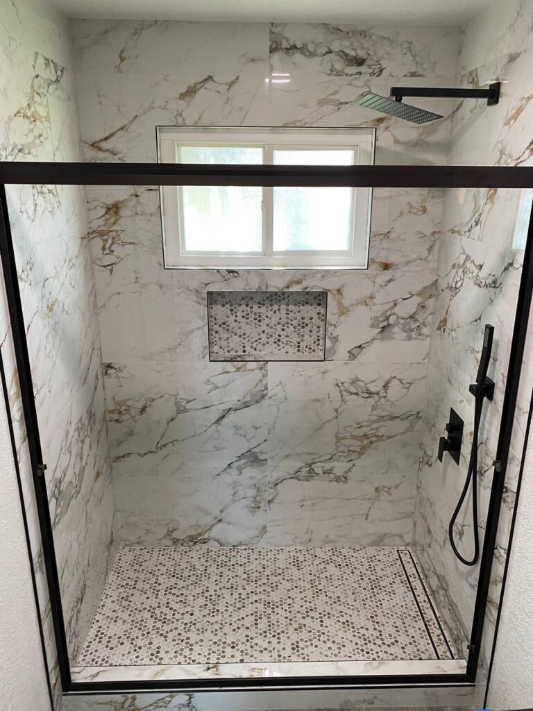 Bright walk-in shower with a glass enclosure, marble-look wall tiles, and a mosaic tiled shower pan in a compact bathroom