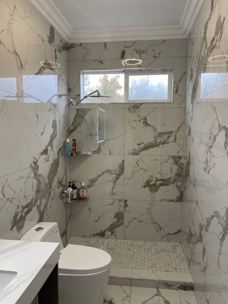 Walk-in shower with a tiled shower pan in a small bathroom space, finished with marble-look wall tiles and modern fixtures