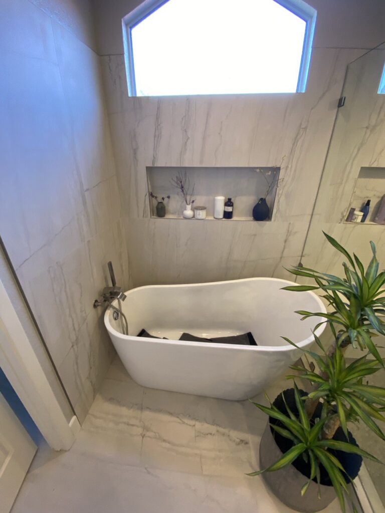 Freestanding bathtub under a geometric window with built-in wall niche in a modern marble-tiled bathroom