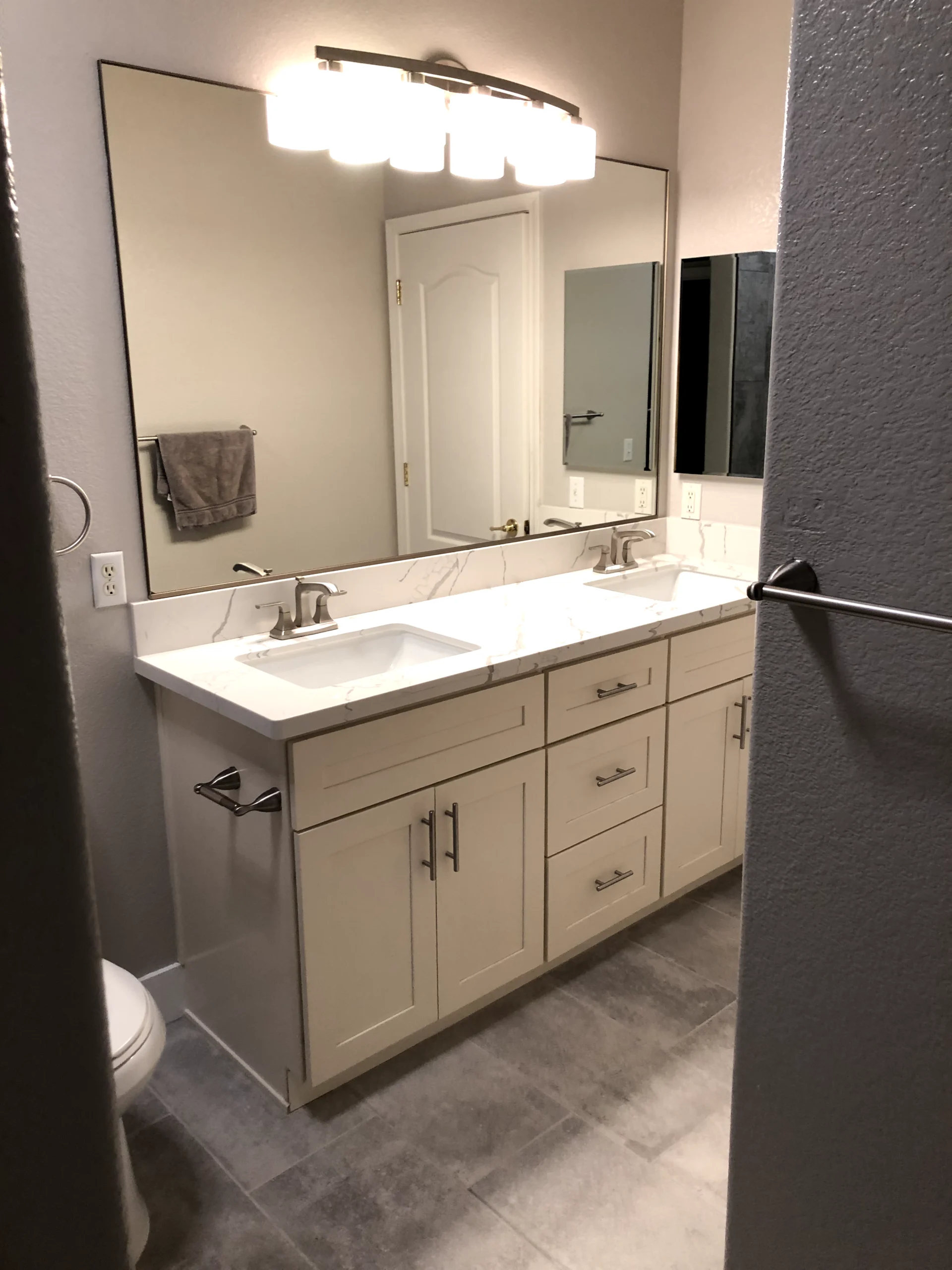 Double vanity bathroom remodel in Folsom with quartz-look countertop, modern lighting, large mirror, and gray tile flooring.