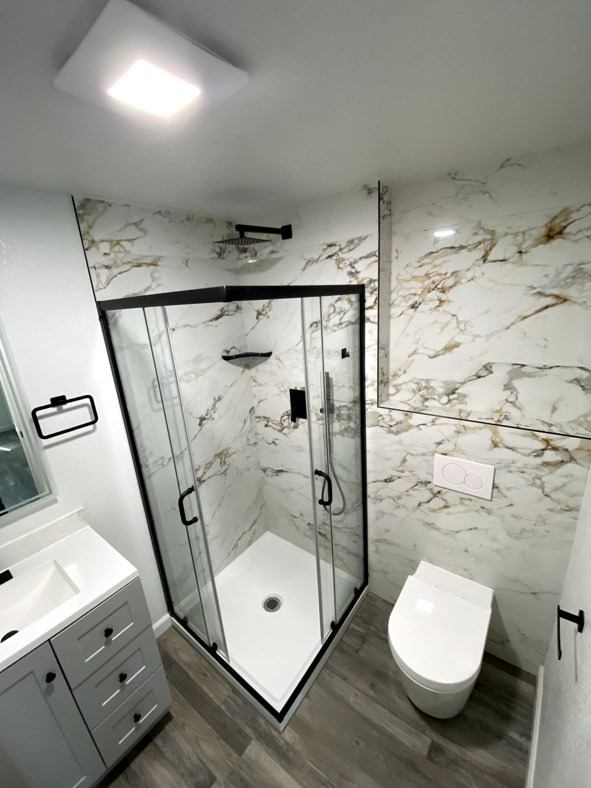 Small bathroom remodel in Granite Bay with marble-look shower walls, glass shower enclosure, black fixtures, and modern vanity.