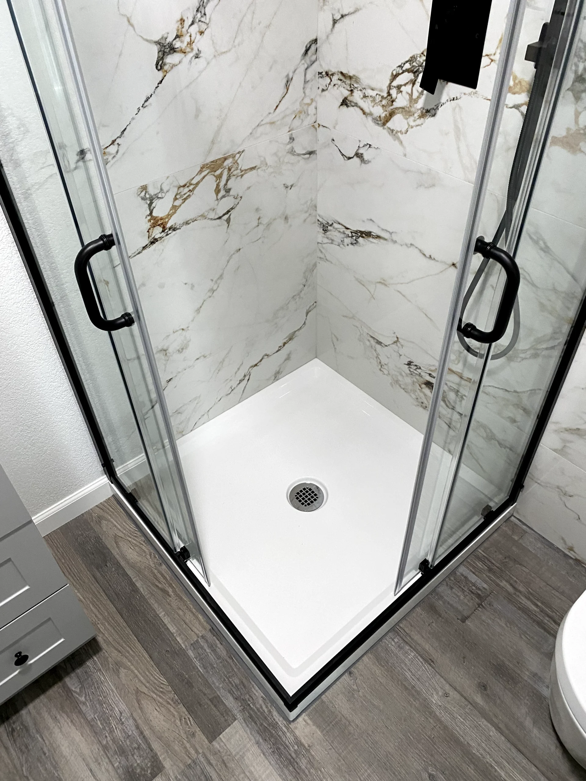 Glass shower enclosure installation in Roseville with marble-look shower panels, black hardware, and clean white shower base.