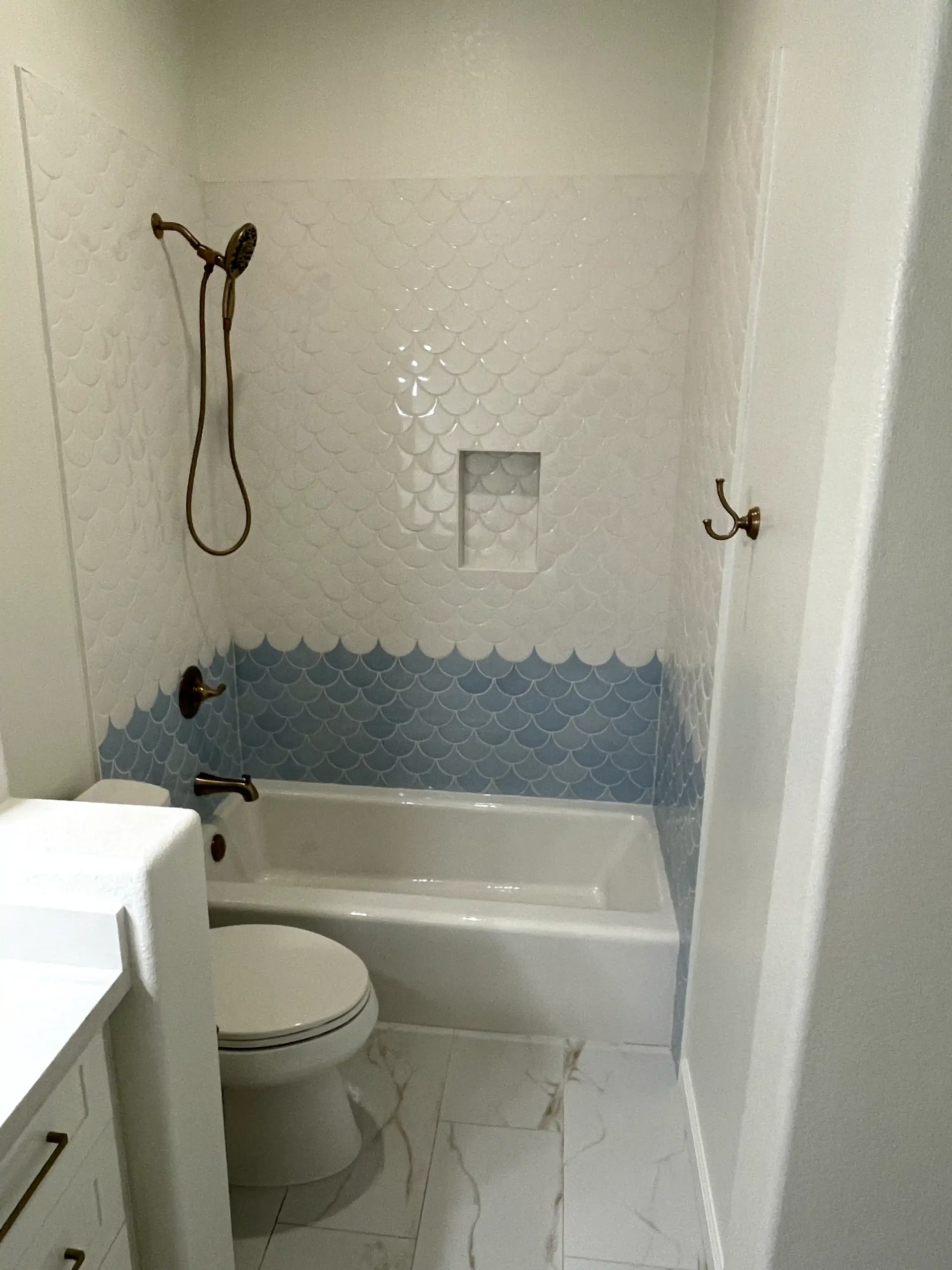 Custom shower tile installation in Sacramento with white scallop tile, blue accent tile, shower niche, bathtub, and brass shower fixtures.