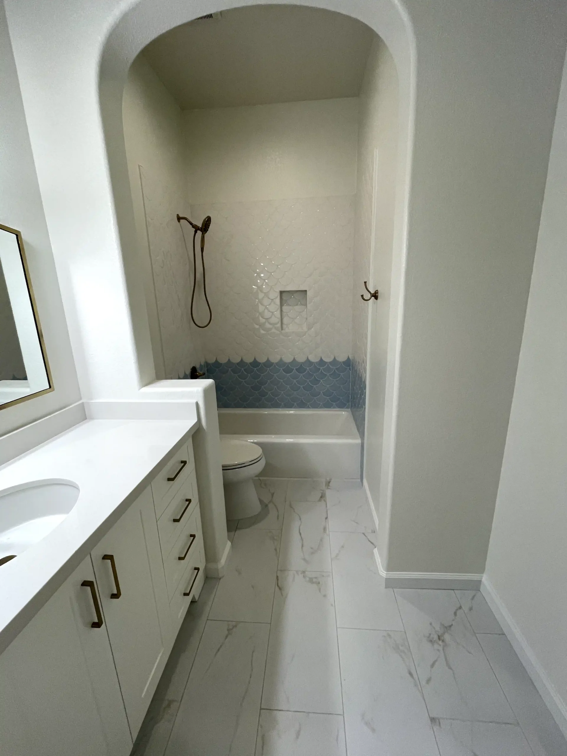 Guest bathroom remodel in El Dorado Hills with white vanity, marble-look floor tile, arched shower opening, blue accent tile, and bathtub.