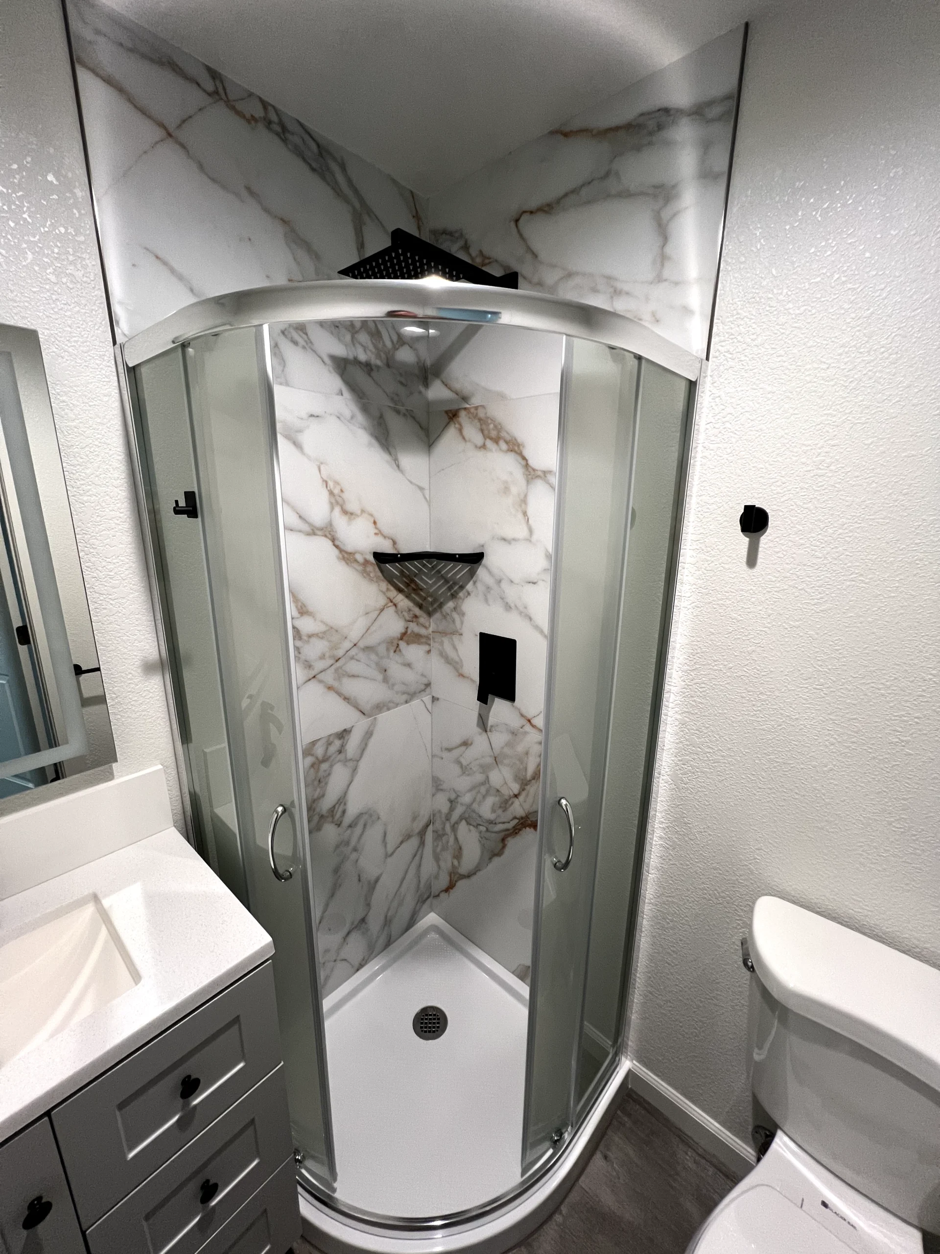 Walk-in shower remodel in Elk Grove with marble-look wall tile, sliding glass door, rainfall shower head, and built-in storage.