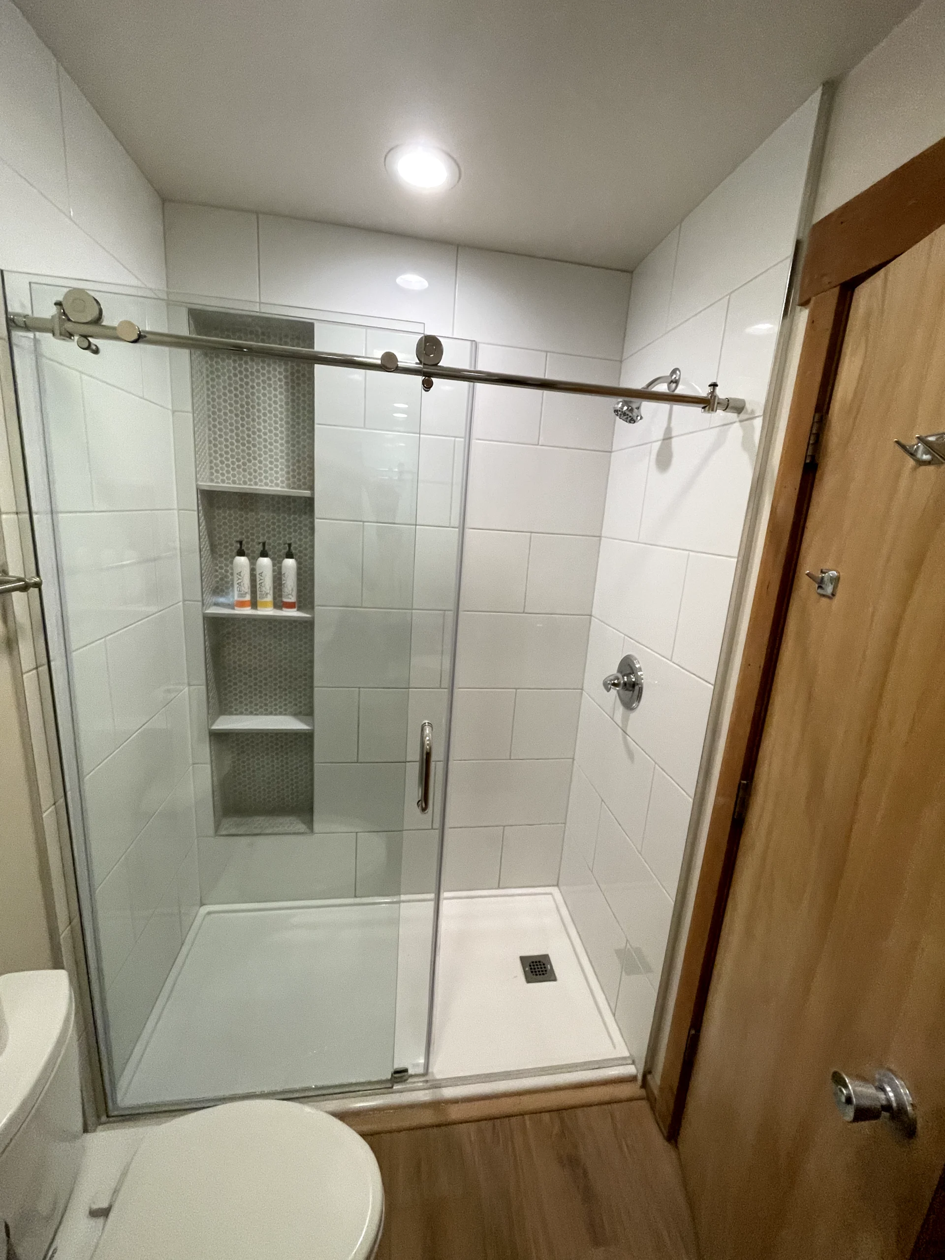 Walk-in shower remodel in Elk Grove with marble-look wall tile, sliding glass door, rainfall shower head, and built-in storage.
