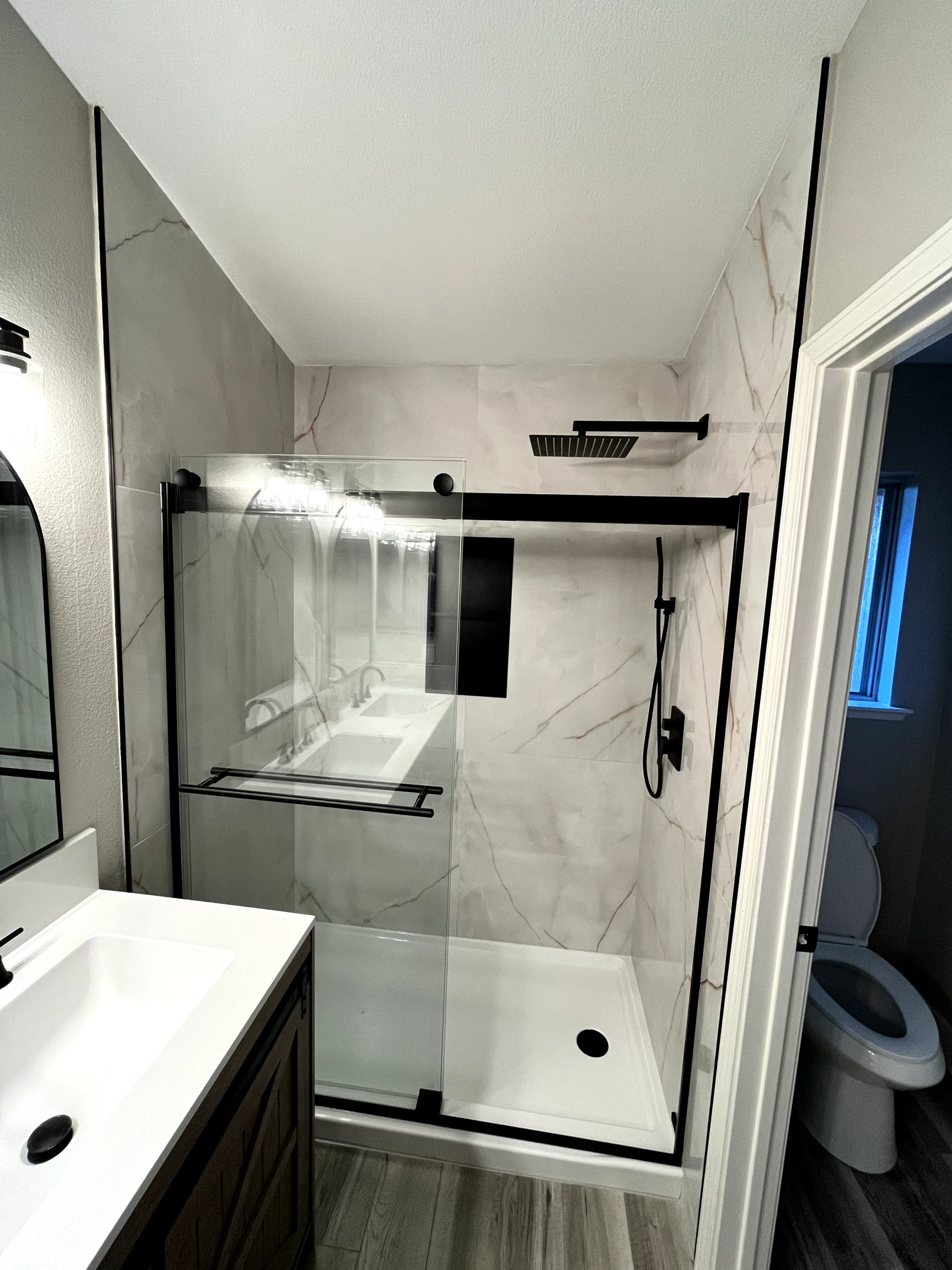 Walk-in shower remodel in Elk Grove with marble-look wall tile, sliding glass door, rainfall shower head, and built-in storage.