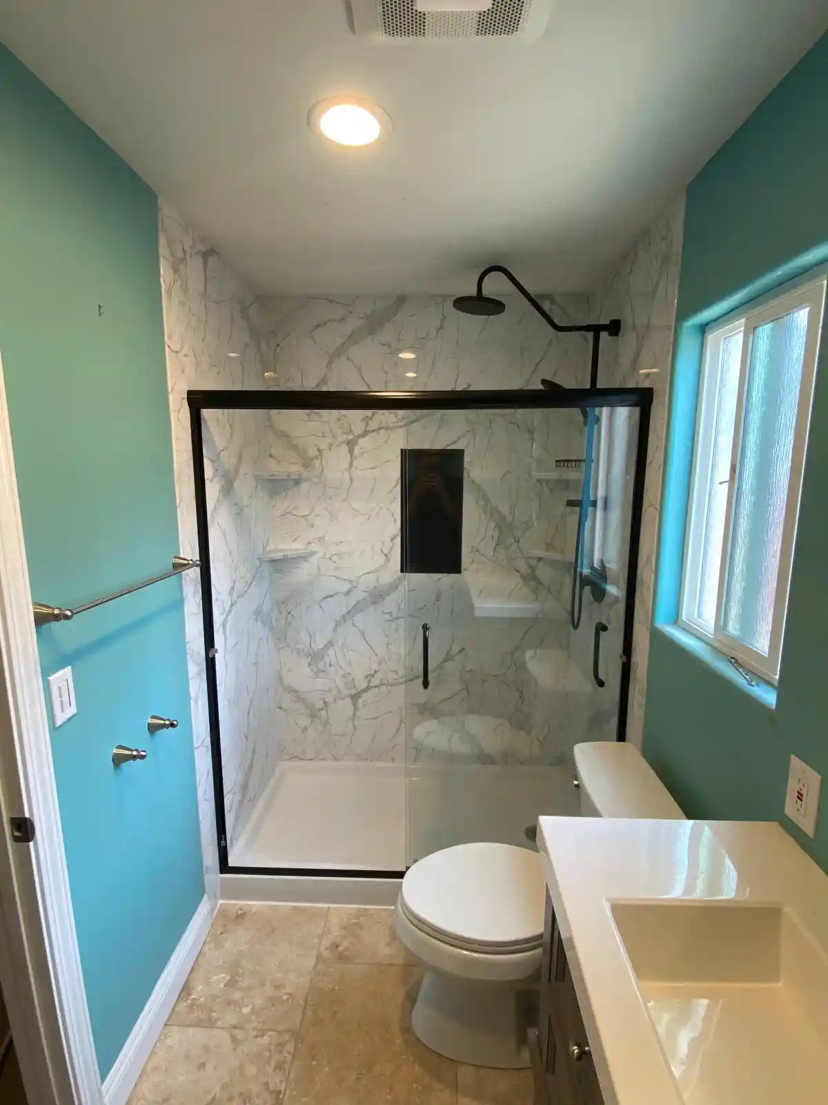 Bathroom wall panel installation in Sacramento with marble-look shower panels, black framed glass shower door, rainfall shower head, and updated vanity.