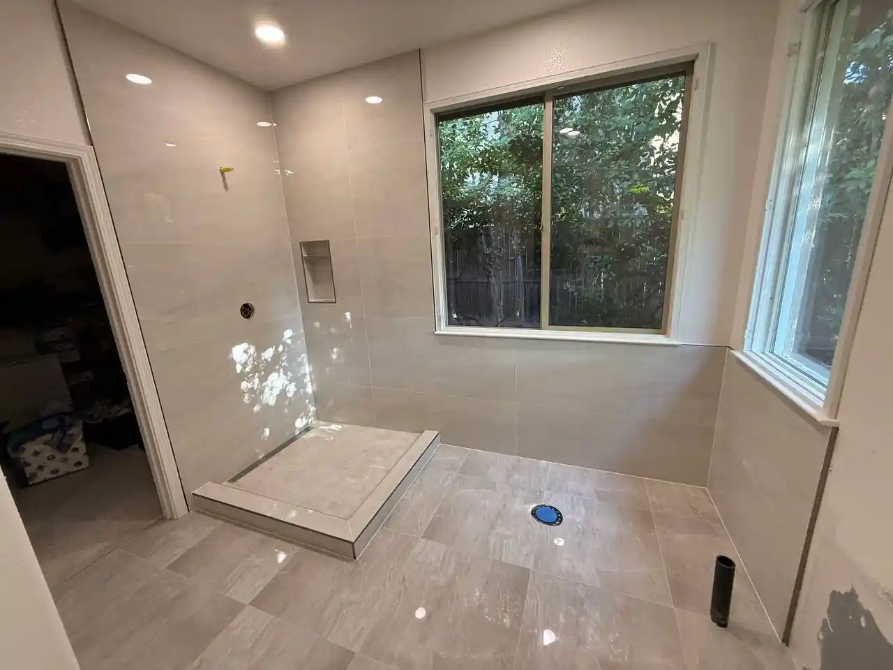 Walk-in shower remodel in Elk Grove with marble-look wall tile, sliding glass door, rainfall shower head, and built-in storage.