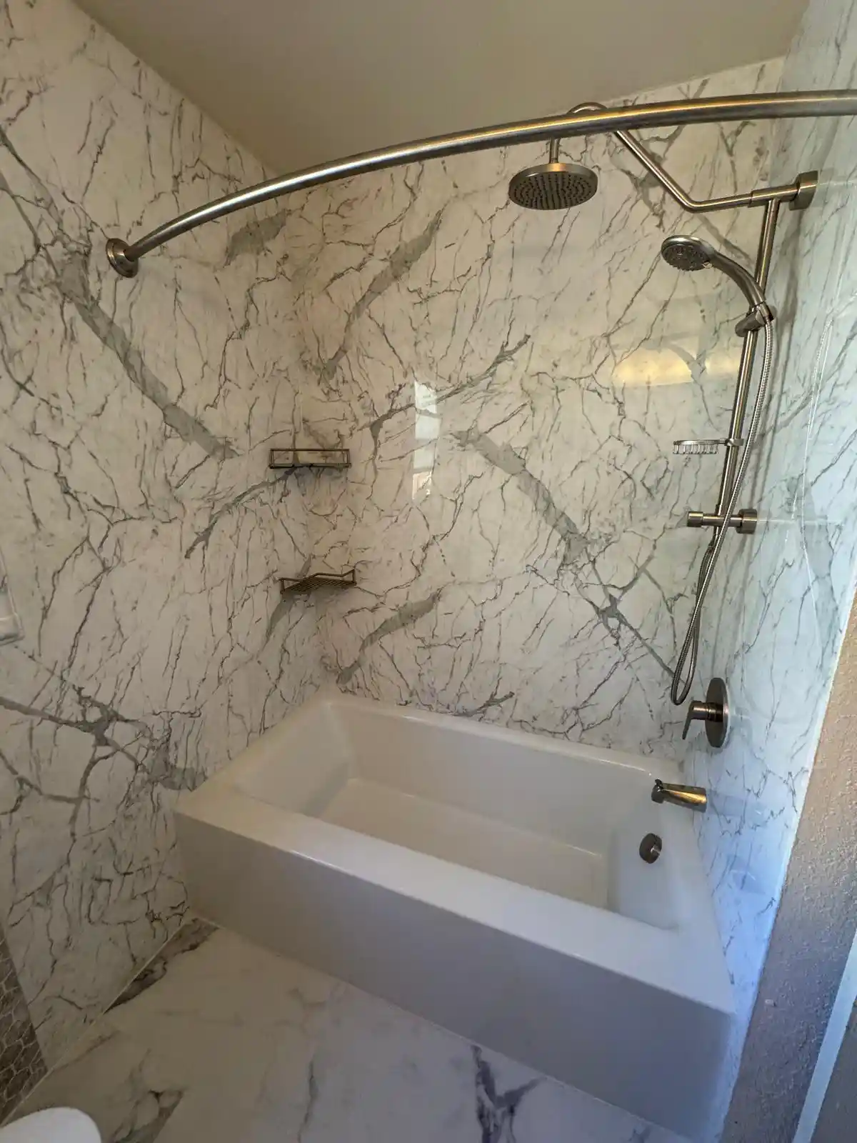 Custom shower tile installation in Sacramento with white scallop tile, blue accent tile, shower niche, bathtub, and brass shower fixtures.